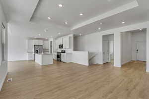 Unfurnished living room featuring light wood-style flooring, a sink, a raised ceiling, and visible vents