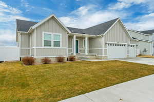 View of front of home with concrete driveway, fence, board and batten siding, a front lawn, and a garage