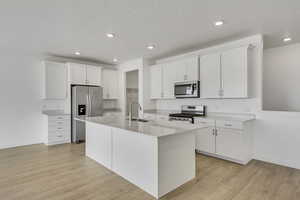 Kitchen with an island with sink, a sink, stainless steel appliances, white cabinets, and light wood-style floors