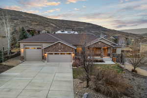 View of front facade with stone siding, an attached garage, roof with shingles, driveway, and a mountain view