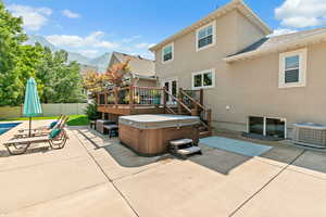 Rear view of house with a deck with mountain view, a patio, a hot tub, stucco siding, and cooling unit