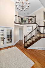 Staircase with baseboards, ornamental molding, wood finished floors, a towering ceiling, and a notable chandelier