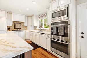 Kitchen with light stone countertops, stainless steel appliances, tasteful backsplash, a sink, and light wood-style floors