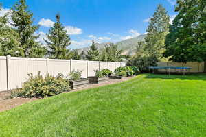 View of yard with a trampoline, a vegetable garden, a mountain view, and fence