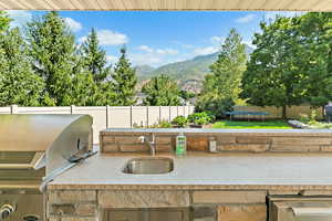 View of patio with exterior kitchen, a trampoline, a fenced backyard, a sink, and a mountain view
