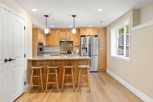 Kitchen featuring under cabinet range hood, a peninsula, light wood-style floors, light stone countertops, and appliances with stainless steel finishes
