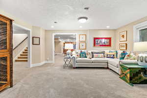 Carpeted living room featuring baseboards, a textured ceiling, recessed lighting, and stairway
