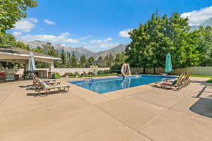 View of swimming pool with a fenced backyard, a water slide, a patio area, and a mountain view