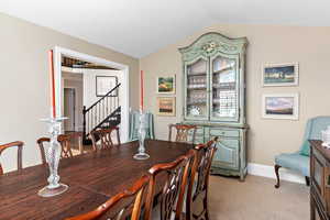 Dining room featuring light colored carpet, baseboards, stairway, and lofted ceiling