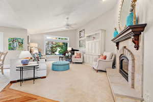 Carpeted living room featuring baseboards, lofted ceiling, a fireplace, and ceiling fan