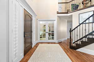 Entryway with french doors, a towering ceiling, stairway, and wood finished floors