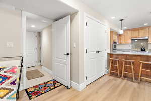 Kitchen featuring oven, under cabinet range hood, backsplash, light stone counters, and light wood finished floors
