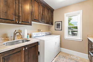 Clothes washing area with washer and clothes dryer, a sink, baseboards, visible vents, and cabinet space