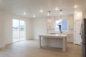Kitchen with light wood-style floors, freestanding refrigerator, decorative backsplash, and baseboards