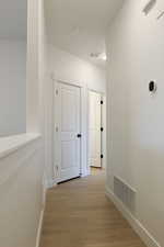 Hall with visible vents, light wood-style floors, and baseboards