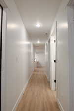 Hallway with visible vents, light wood finished floors, and baseboards