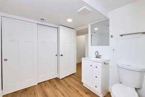 Bathroom with toilet, vanity, wood finished floors, a textured ceiling, and visible vents