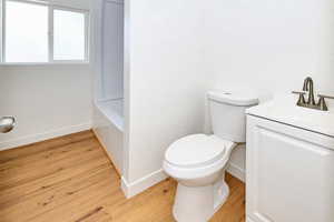 Full bath with a washtub, baseboards, toilet, wood finished floors, and vanity
