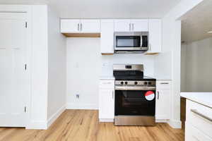 Kitchen with white cabinets, light countertops, appliances with stainless steel finishes, and light wood-type flooring