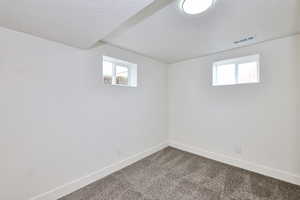 Below grade area with a textured ceiling, visible vents, plenty of natural light, and dark colored carpet