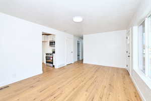 Empty room with baseboards, a textured ceiling, visible vents, and light wood-type flooring