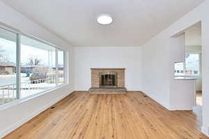 Unfurnished living room with a textured ceiling, a stone fireplace, light wood-type flooring, baseboards, and visible vents