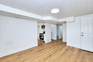 Spare room featuring baseboards, a textured ceiling, light wood-style flooring, and visible vents