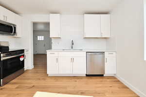 Kitchen with white cabinets, light wood finished floors, stainless steel appliances, tasteful backsplash, and a sink