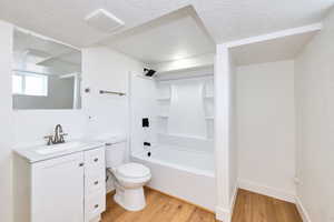 Bathroom featuring toilet, vanity, wood finished floors, a textured ceiling, and visible vents