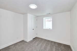 Carpeted empty room featuring baseboards, a textured ceiling, and visible vents