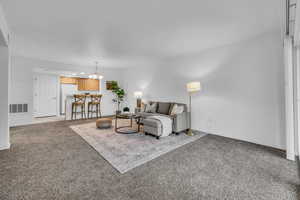 Living area featuring baseboards, carpet flooring, visible vents, and a notable chandelier