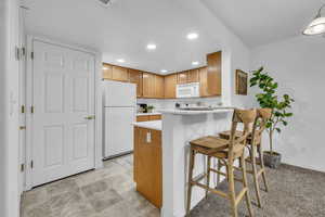 Kitchen with light countertops, a peninsula, white appliances, recessed lighting, and brown cabinetry