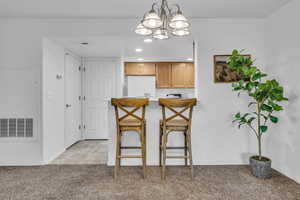 Kitchen with decorative light fixtures, a notable chandelier, visible vents, freestanding refrigerator, and light carpet