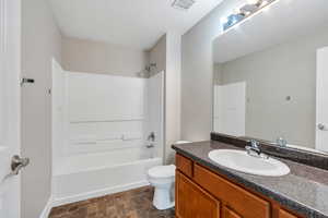 Full bath with toilet, vanity, shower / bathtub combination, stone finish flooring, and baseboards