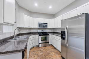 Kitchen featuring stainless steel appliances, a sink, stone finish floors, white cabinets, and recessed lighting