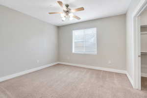 Unfurnished bedroom with a walk in closet, light carpet, a closet, baseboards, and ceiling fan