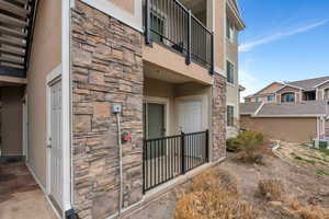 View of exterior entry with stone siding, a balcony, stucco siding, and central AC unit