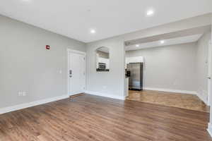 Unfurnished living room with arched walkways, dark wood finished floors, baseboards, and recessed lighting
