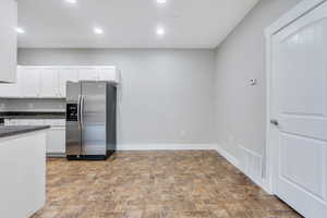 Kitchen with stainless steel fridge with ice dispenser, dark countertops, stone finish flooring, white cabinetry, and baseboards