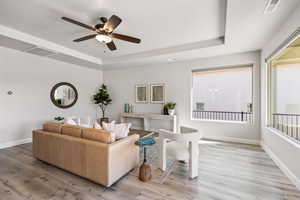 Living area featuring a tray ceiling, a ceiling fan, light wood-style floors, and baseboards