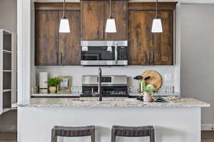 Kitchen featuring stainless steel appliances, an island with sink, dark brown cabinetry, a kitchen bar, and a sink