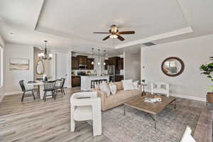 Living area featuring a raised ceiling, light wood finished floors, baseboards, and ceiling fan