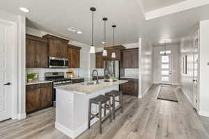 Kitchen with stainless steel appliances, a sink, light wood-type flooring, dark brown cabinetry, and recessed lighting