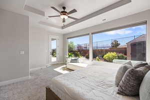 Bedroom featuring a tray ceiling, access to exterior, baseboards, carpet floors, and a ceiling fan