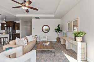 Living area featuring a tray ceiling, a ceiling fan, baseboards, and wood finished floors