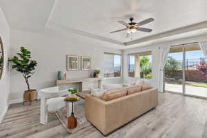 Living room featuring a tray ceiling, light wood-style flooring, ceiling fan, and baseboards