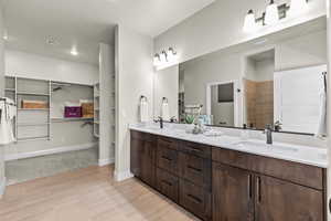Bathroom featuring a spacious closet, double vanity, baseboards, a tile shower, and wood finished floors