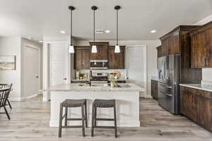 Kitchen featuring stainless steel appliances, a sink, light wood-style flooring, dark brown cabinetry, and a breakfast bar