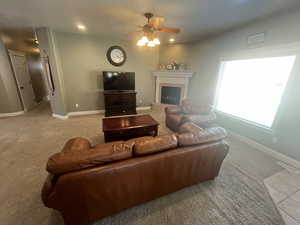 Carpeted living room featuring a ceiling fan, a tiled fireplace, and recessed lighting