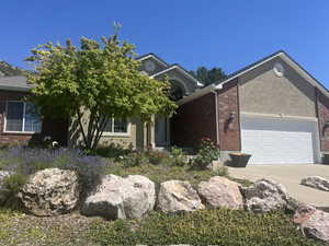 View of front of house with driveway, an attached garage, brick siding, and stucco siding
